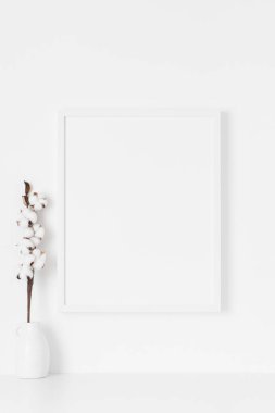 Beyaz çerçeve, pamuk dallı bir dekorasyonla duvarda..