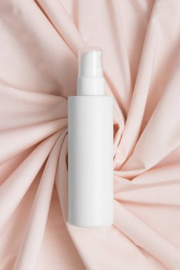 Beyaz kozmetik losyon şişesi yumuşak pembe tekstil üzerinde..
