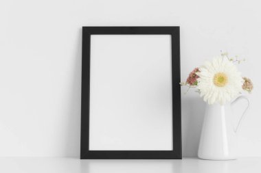 Beyaz masada bir buket çiçekli siyah çerçeve..