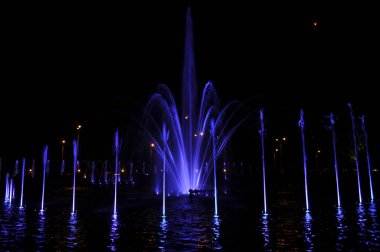 Çeşme suyu, gece mavisi ışıklarda halka halinde uçar.