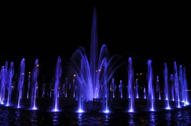 Çeşme suyu, gece mavisi ışıklarda halka halinde uçar.