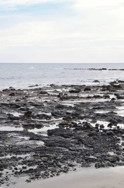 Volkanik siyah kayalar ve bulutların altında karamsar deniz