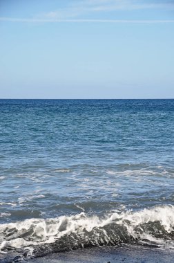 Mavi deniz ufku ve siyah çakıl taşı plajı;