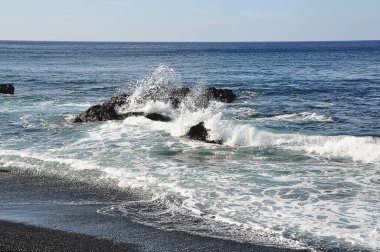 Dalgalar kızıl kayalara ve mavi denize çarpıyor;