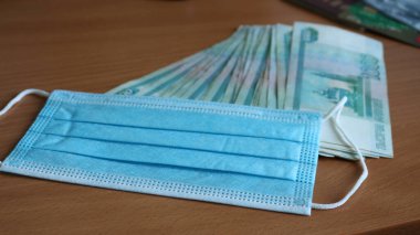 Tek kullanımlık koruyucu bir maskeyle kaplı 1000 rublelik Rus banknotları bankanın plastik kartlarının bulanık arka planında, ahşap bir masanın üzerinde uzanıyordu.