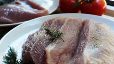 Dilimlenmiş taze çiğ hindi filetosu, pürüzsüz et dokusu ve yapıda sulu yağ, arka planda olgun domatesler ve dereotlu büyük bir tabakta kesilmiş kümes hayvanları eti.