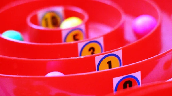red plastic board game with number markings of points on circular paths along which colorful balls roll chips for family fun, illustration of the distribution of seats with emphasis on the number one