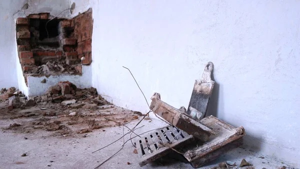 a disassembled antique fireplace or stove in an old house and iron parts from its structure - fittings, wires, a barrier among brick chips on the floor against a background of a bleached wall