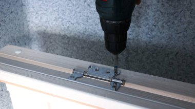 Gri duvarların arka planına karşı hafif ahşap bir kapı çerçevesi üzerinde metal vidalara vidalanan matkap yakın çekim, kurulum için kapı çerçevesi hazırlama süreci