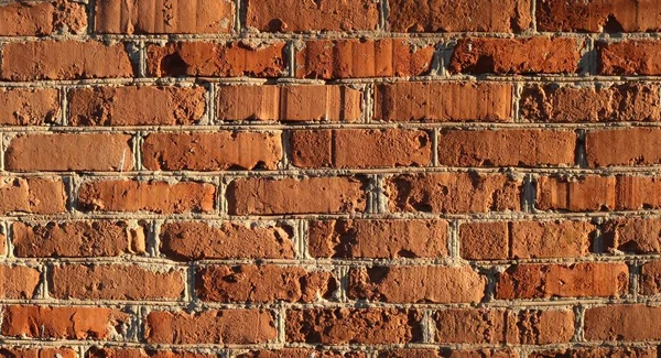 薄いコンクリートの縫い目と明るいオレンジ色のブロックの不均一な石積みのレンガの壁の断片 柔らかい日差しに照らされた完全なフレーム抽象的なテクスチャレンガの背景 — ストック写真