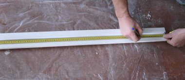 Kapı eğiminin uzunluğunu ölçerken bir mezura ile elle çalışma, oda kapılarının dış şeritlerini kurarken işçinin elindeki mezura paneli