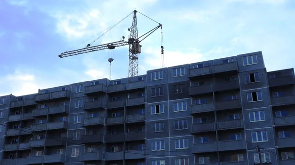 a construction crane visible behind an unfinished apartment building without finishing with inserted plastic windows, completing the construction of a residential complex in the evening at sunset