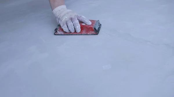 一只手戴在手套上 用磨碎的翡翠工具擦去斑斑表面的粗糙和不规则 修理房屋墙壁的背景 — 图库照片