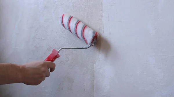 textured wall to which wallpaper glue is applied using a bright roller, renovation background with the image of a man\'s hand with a striped roller on the background of an empty surface