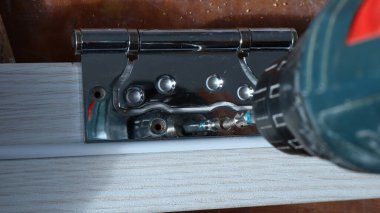 Aydınlık ahşap şeritte delikleri olan parlak metal bağlayıcı aletin baskısı altında kendini tıkayan vidayı kendi kendine takıyor. Kapı menteşesine vidaları vida ve tamir yakın plan