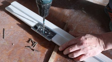 Kapı çerçevesini monte etmek için bir tornavida, kapı çerçevesini yerleştirmek için bir marangozun işi olan hafif ahşap şeritteki metal bir deliğe kendi kendine dokunan vidayı vidalamak.