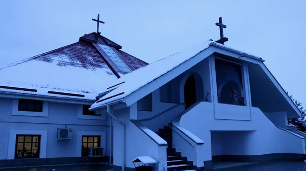 a white Protestant church in winter twilight with the sivols of Christianity in the form of small simple crosses on the roof, sprinkled with snow, religious restrained architecture in the dark evening darkness