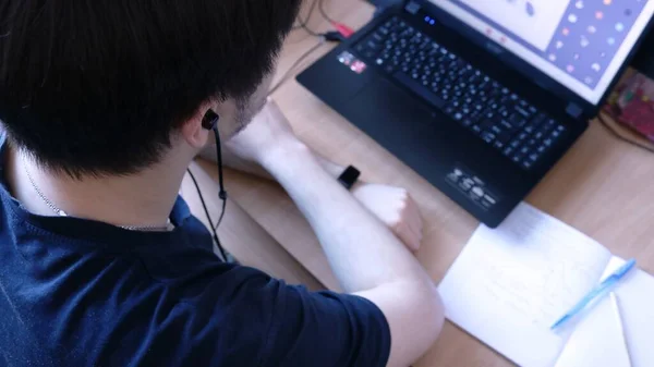 a student in an online lesson on video communication sitting at a home table in front of a working laptop monitor, distance education and remote presence at lessons and lectures