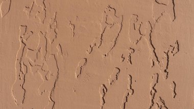 Dekoratif alçı yüzeyinde soyut girintilerle şeftali bej tonunun dokuları, gölgeli düzensizliklerle duvarın detaylı dokusu ve vurgunların aydınlatılması.