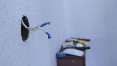 Evin elektrik prizinde açık dairesel bir delik mavi elektrik bandıyla kaplı iki kablo ile bir odanın köşesinin bulanık arka planına ve rafta duran aletlere karşı.