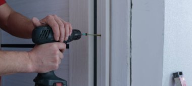 Erkek çalışan eller bir tornavida ile kapı eğimli ahşap şerit vidalama, iç yenileme sürecinde kapı çerçevesi monte ve onarım