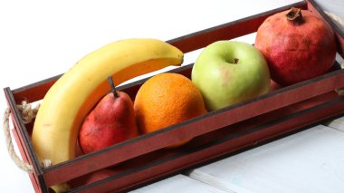 Beyaz bir yüzey üzerinde parlak meyveler olan dar bir dekoratif kutu çapraz olarak üst görünümde, farklı türde meyveler beyaz bir masanın üzerinde duran ahşap bir kutuda istiflenmiştir.