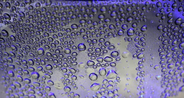 purple large drops on a wet transparent surface as an abstract textured macro background, evaporation of water and the deposition of condensate on the glass in the illumination of purple backlight close-up