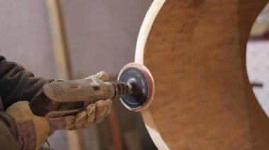 Bir marangozun elindeki aşındırıcı tekerlekle bir atölyenin bulanık arka planına karşı içi boş bir ağaç gövdesiyle çalışmak ahşap bir parçanın yüzeyini zımparalamak, el yapımı mobilyalar yapmak, marangozluk prodüksiyonunda çalışmak.