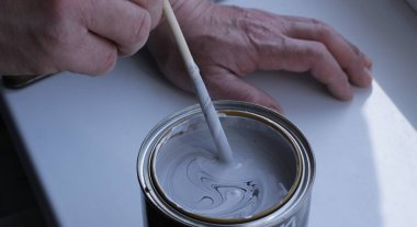stirring paint with a color scheme until a homogeneous mass is obtained by hand with a thin stick close-up, diluting the desired shade of paint in a tin can standing on a white surface clipart