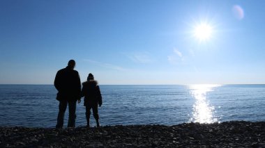 Baba ve oğul, güneşli bir günde soğuk okyanus kenarında yürüyüş yapan bir adam ve bir çocuk, soğuk bir kış manzarasında kayalık bir sahilde bir aile, açık bir gökyüzünün arkaplanına karşı kışın mavi denizle karşı karşıya duruyorlar.