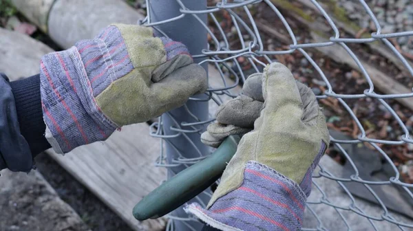 fixing the galvanized mesh to the base of the post when installing the fence in the open air, the hands of the installer wearing thick gloves with pliers tighten the fixing wire fixing the mesh of the fence