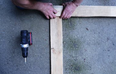 top view of joining two wooden planks on the asphalt surface with a carpenter's kicks with a black screwdriver set aside, the process of a home male carpentry work using a construction tool