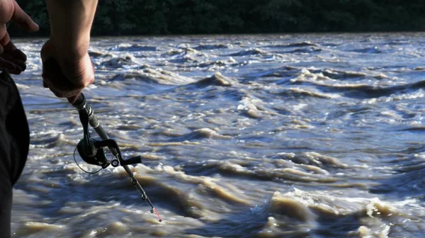 釣り棒を持つ部分的に見える漁師は 急いでストリームと嵐の泥だらけの川の背景に立っています コピースペースとぼやけた焦点で山の川に極端な釣り — ストック写真