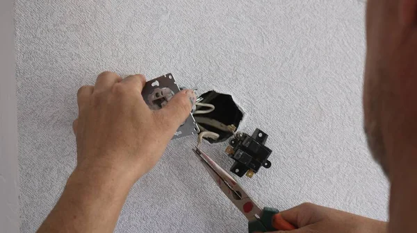 repairing and replacing an electrical wall switch with pliers in the hands of an electrician, focus on the switch being repaired and a blurry image of a worker