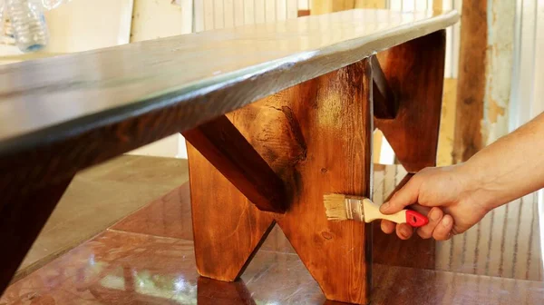 applying varnish on a wooden bench standing on a work table in a carpenter\'s workshop, varnishing a wooden product by hand, manual lacquering of handmade furniture, processing with a protective varnish a bench made of wood
