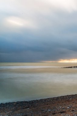 Bir çakıl taşı plajı ve okyanusun uzun pozlu fotoğrafı.