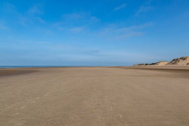 Merseyside 'daki Formby' deki engin kumlu plajda mavi bir gökyüzü var.