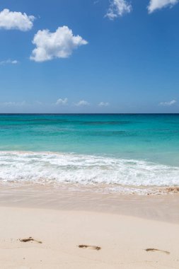 Arkasında turkuaz bir okyanus olan kumlu bir sahilde ayak izleri.