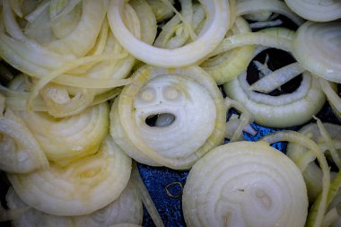 Chopped onions in a pan with one slice looking like a face clipart