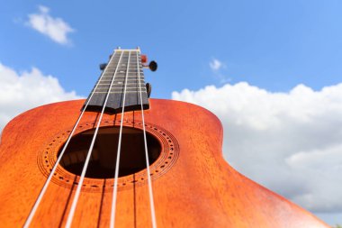 Ahşap ukulele Mavi gökyüzü ve arkasında bulutlar.