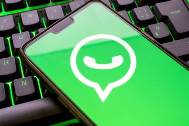 Ekranında yeşil Whatsapp logosu olan cep telefonu ve renkli ışıklandırılmış klavye. Ekranda sembol olan mesajlaşma uygulamasını kullanarak akıllı telefon kavramı