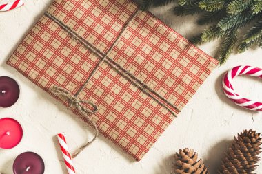 Kareli el sanatları kağıdına sarılı bir Noel hediyesi. Üzerinde mumlar ve süslemeler var.