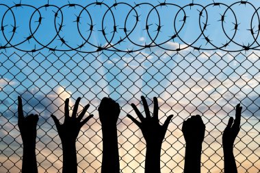 Mülteci ellerini siluet yakınındaki dikenli tel çit.
