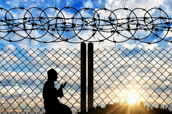 Silhouet vluchteling bidden in de buurt van het hek — Stockfoto