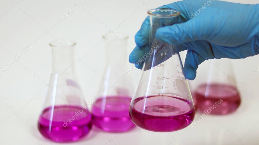 The scientist wear blue nitrile gloves holding Erlenmeyer Conical flask, with purple violet solvent forming reaction boric acid and ammonia solution analysis in wastewater sample. Selective focus.