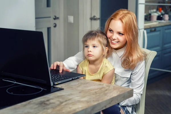 beautiful red-haired girl teenager teaches her little sister to use a laptop. e-learning