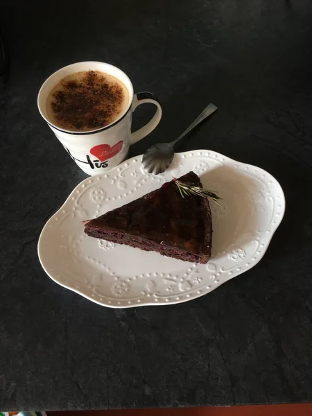 Xícara de cappuccino e torta de cereja de chocolate na placa branca no fundo preto — Fotografia de Stock