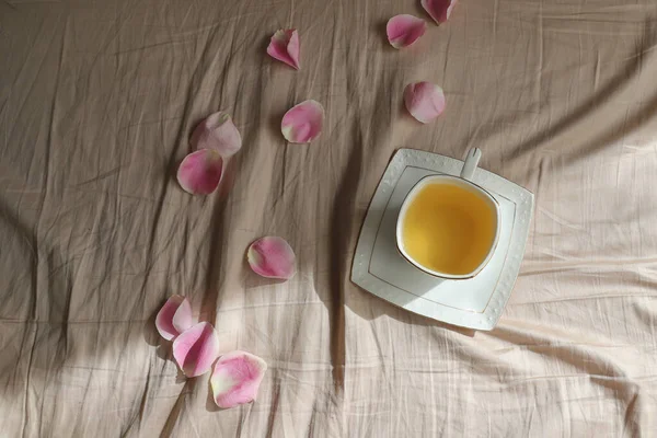 Ένα φλιτζάνι τσάι με ροδοπέταλα στο σεντόνι, πρωινό στο κρεβάτι για την αγαπημένη σας — Φωτογραφία Αρχείου