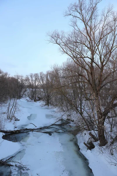Μικρό στενό ποτάμι καλυμμένο με πάγο και χιόνι που περιβάλλεται από δέντρα, ρουστίκ χειμώνα τοπίο — Φωτογραφία Αρχείου
