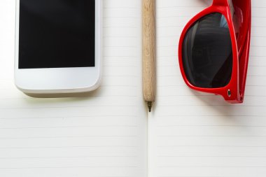 Defter, kalem, güneş gözlüğü ve cep telefonu